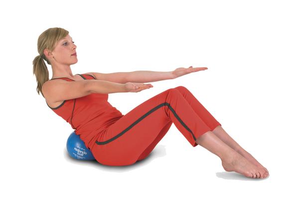 Frau in rotem Sportoutfit macht Rückenübung auf blauem Gymnastikball vor weißem Hintergrund.