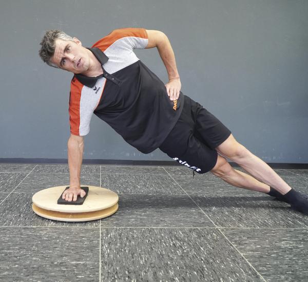 Mann macht seitlichen Unterarmstütz auf Balance-Board zur Kräftigung der Rumpfmuskulatur.
