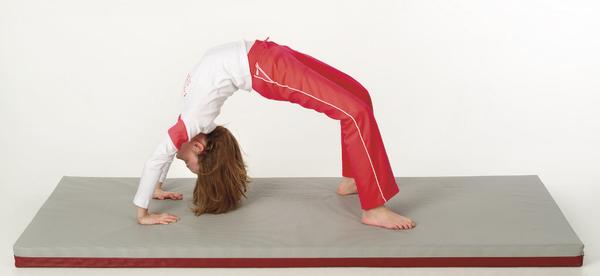 Kind macht Rückwärtsbrücke auf Gymnastikmatte in Sportkleidung vor weißem Hintergrund