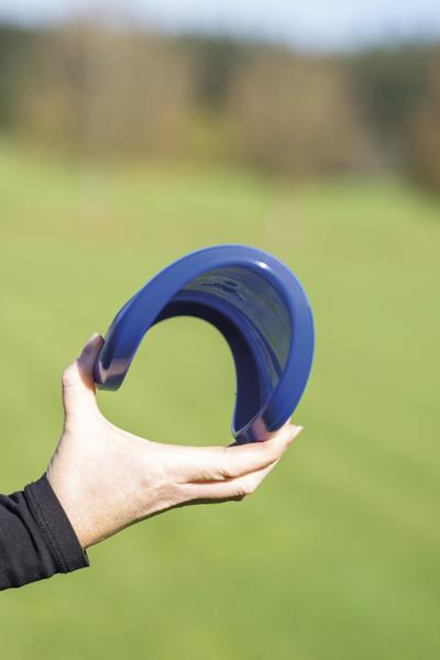 Hand hält gebogenen blauen Kunststoffbogen vor unscharfem grünen Hintergrund.