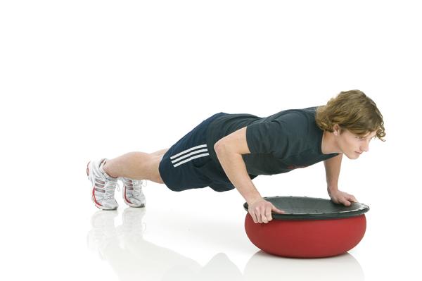 Mann macht Liegestütze mit Händen auf einem halben Balance-Trainingsgerät.