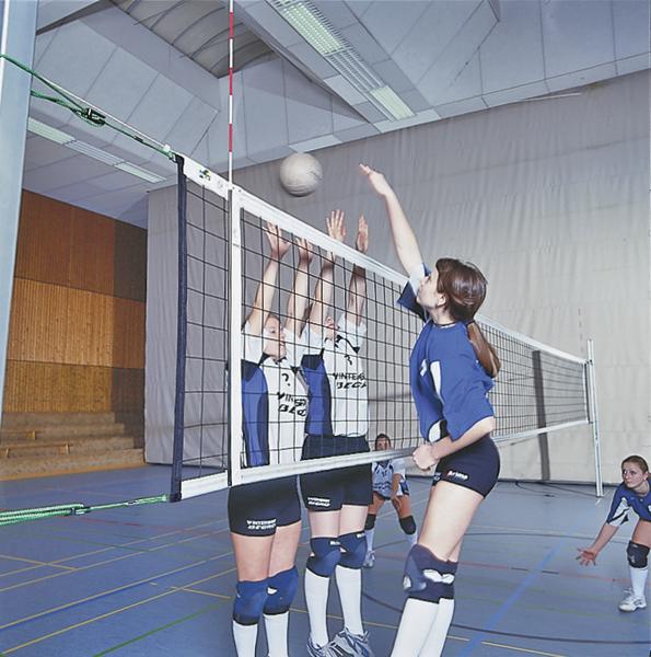 Junge Volleyballspielerinnen blocken und schlagen den Ball in der Halle während eines Spiels.