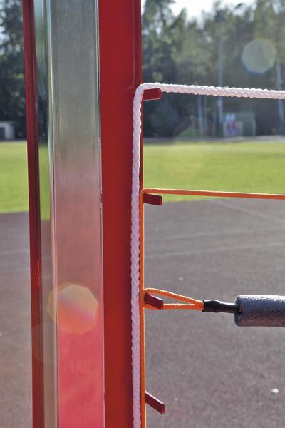 Nahaufnahme eines Volleyballnetzes mit rotem Pfosten auf einem Sportplatz bei Sonnenschein.