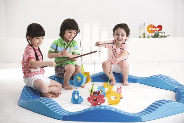 Drei Kinder spielen mit magnetischen Angelspielzeug im blauen Spielbereich auf weißem Boden.