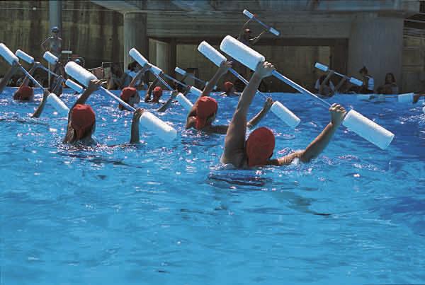 Wassergymnastik-Gruppe mit roten Badekappen und Schaumstoffhanteln im Schwimmbecken.