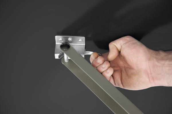 Hand dreht Griff an Metallhalterung zur Befestigung an schwarzer Wand.
