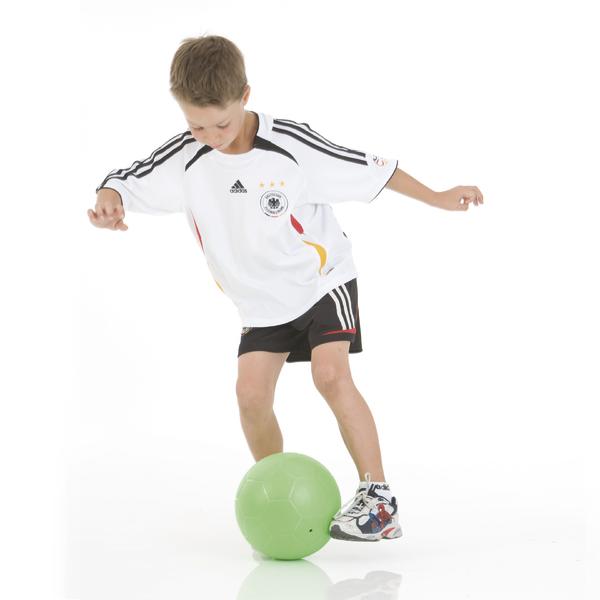 Junge in Deutschland-Fußballtrikot spielt mit grünem Ball auf weißem Hintergrund.