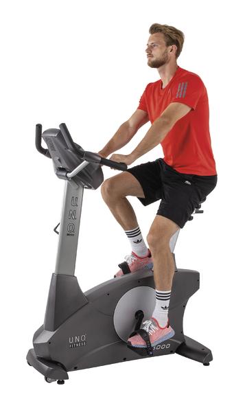 Mann trainiert auf stationärem Fahrrad in rotem Shirt und schwarzer Sporthose vor weißem Hintergrund.