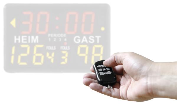 Hand hält Fernbedienung vor digitaler Sportanzeige mit Spielstand und Spielzeit.