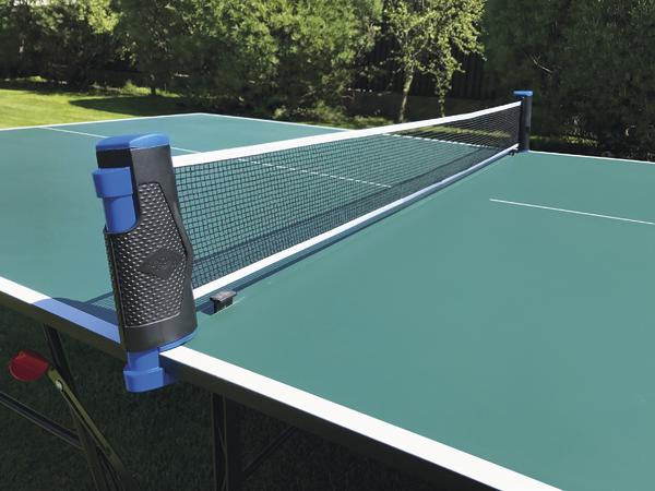 Outdoor Tischtennisplatte mit Netz und grünem Spielfeld im Garten bei Sonnenschein.