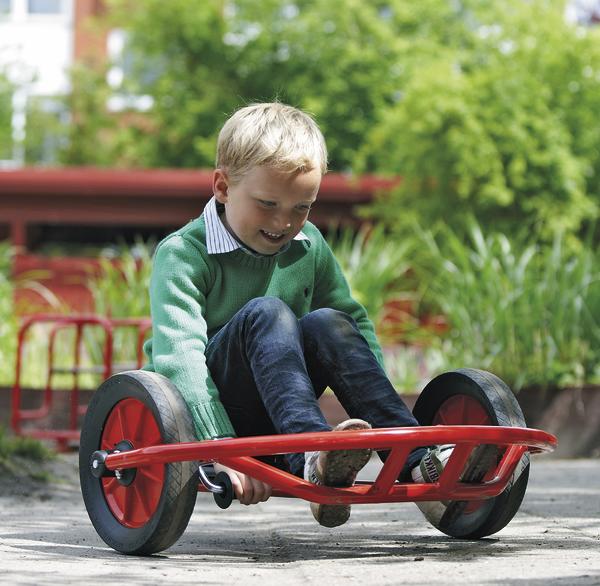 Junge fährt mit rotem Pedal-Kart im Freien auf einem Weg bei sonnigem Wetter.