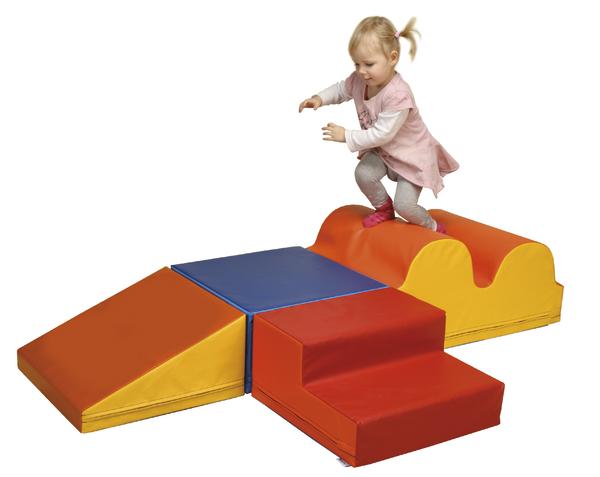 Kleines Mädchen spielt auf buntem Kletter- und Spielset aus Schaumstoff im Innenbereich.