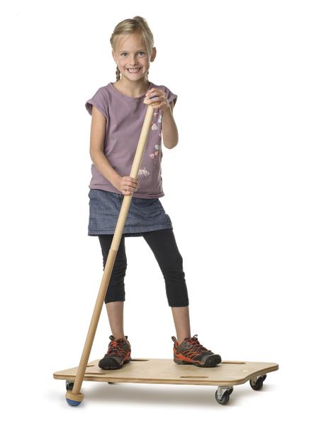 Mädchen steht auf Rollbrett und hält langen Stock, lächelnd vor weißem Hintergrund.