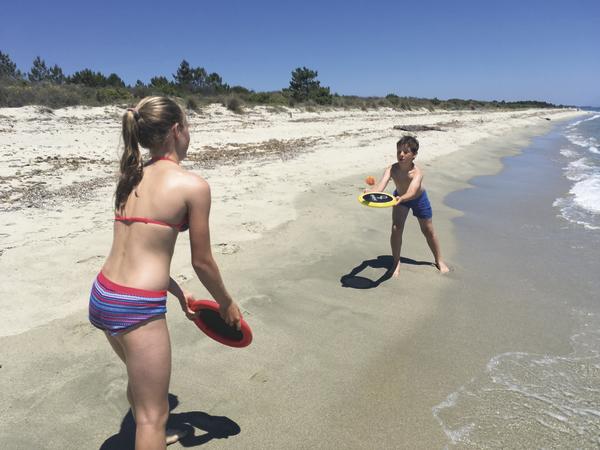 Kinder spielen mit Wurfspielzeug am sonnigen Sandstrand neben dem Meer.