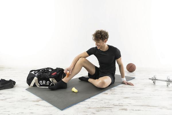 Mann in Sportkleidung massiert nach dem Training seine Wade auf Yogamatte im Fitnessraum.