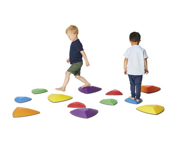 Zwei Kinder balancieren auf bunten, rutschfesten Spielsteinen auf weißem Hintergrund.