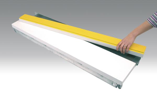 Hand entfernt gelbe Schutzfolie von weißem Kunststoffprofil auf grauem Hintergrund.