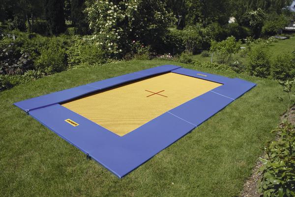 Bodentrampolin mit blauem Rand und gelber Sprungfläche im grünen Garten.