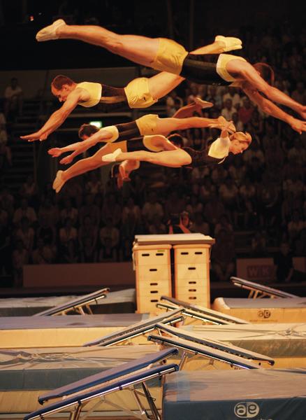 Akrobaten springen synchron über Trampoline bei einer Turnshow vor Publikum.