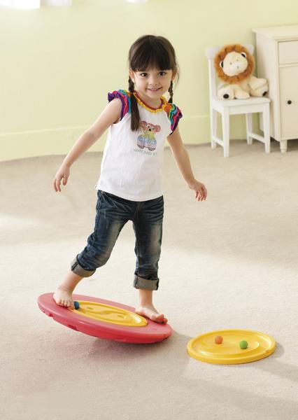 Mädchen balanciert spielerisch auf einem bunten Wackelbrett im hellen Kinderzimmer.