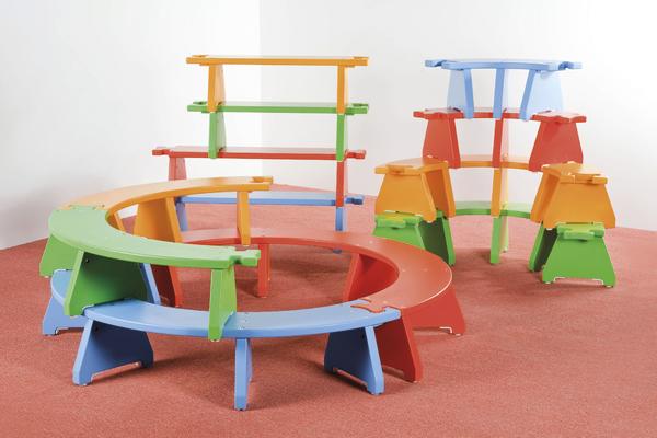 Bunte Puzzlebänkchen, bestehend aus Tischen und Sitzbänken auf rotem Teppich.