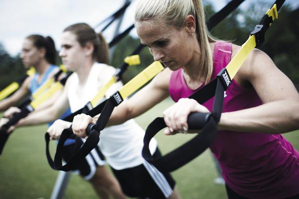 Frauen trainieren mit TRX-Bändern im Freien für Kraft und Ausdauer.