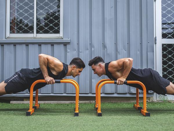 Zwei Männer machen Liegestütze an parallelen Barren im Outdoor-Fitnessbereich.
