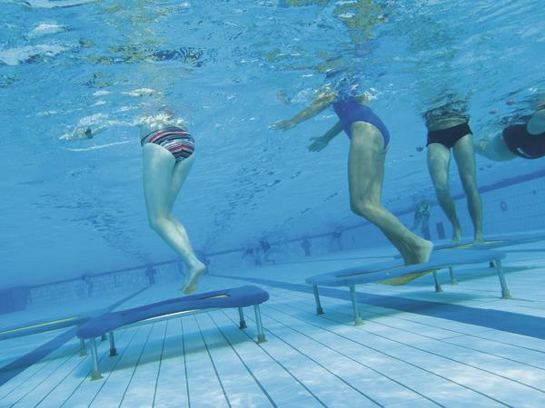 Unterwasseraufnahme von Menschen beim Aquafitness-Training auf Bänken im Schwimmbecken.