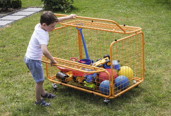 Kind schiebt orangenes Spielzeug-Aufbewahrungsnetz mit Bällen und Spielzeug im Garten.