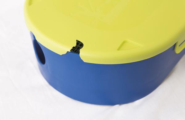 Nahaufnahme eines runden Behälters mit blauem Unterteil und neongelbem Deckel mit kleiner Aussparung.