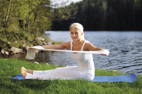 Frau macht Dehnübungen mit Gymnastikband am Seeufer auf Yogamatte im Freien.