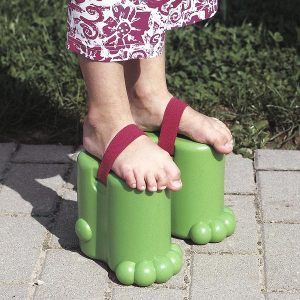 Grüne Kinder-Holzstelzen mit roten Bändern auf Pflastersteinen, getragen von einem Kind.