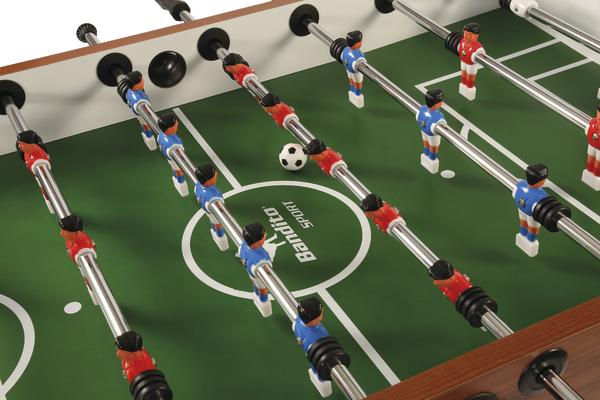 Tischfußballspiel mit roten und blauen Figuren auf grünem Spielfeld und Ball in Spielfeldmitte.