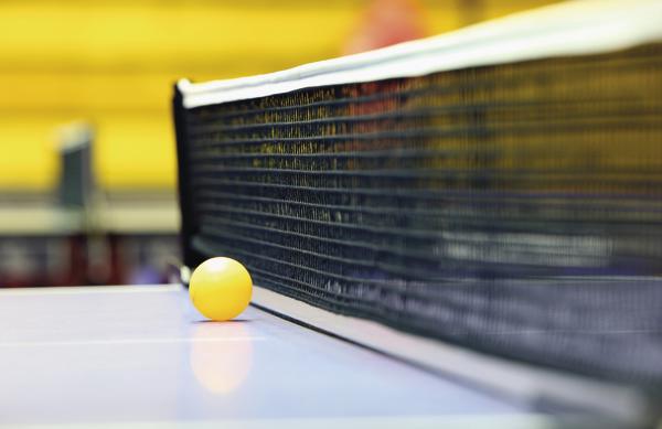 Gelber Tischtennisball liegt am Netz auf dem Tischtennistisch in Sporthalle.
