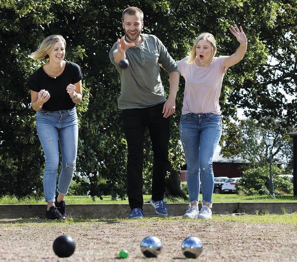 Drei Personen spielen Boule im Freien und werfen Kugeln in Richtung Zielkugel.