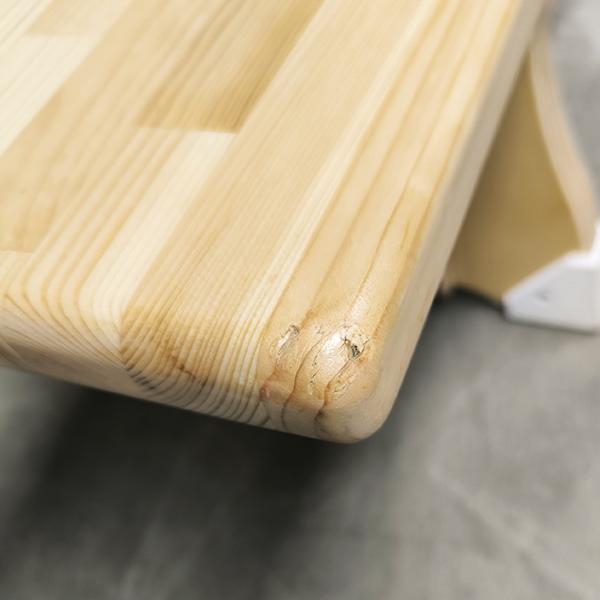 Nahaufnahme einer abgerundeten Holzplatte mit sichtbarer Maserung und kleiner Beschädigung am Rand.