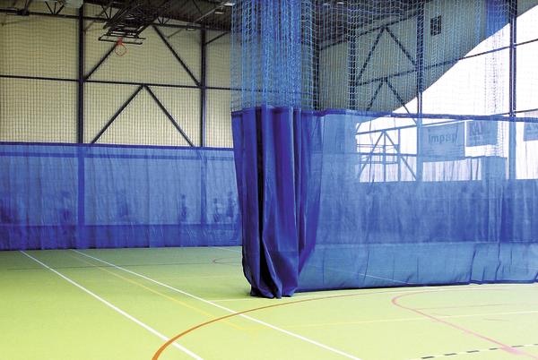Leere Sporthalle mit grünem Boden und blauen Trennnetzen für verschiedene Sportarten.