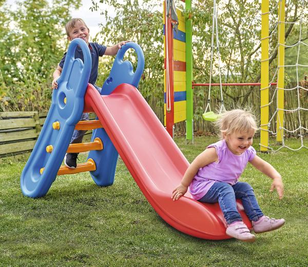 Kind spielt auf roter Rutsche im Garten mit Klettergerüst und grünem Gras.