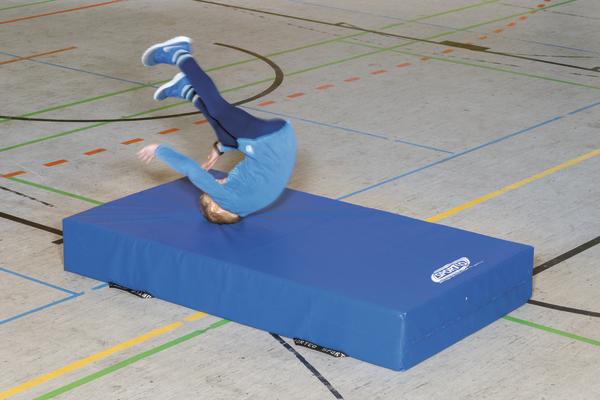 Kind macht Rückwärtsrolle auf blauem Turnmatte in Sporthalle mit Linienmarkierungen.