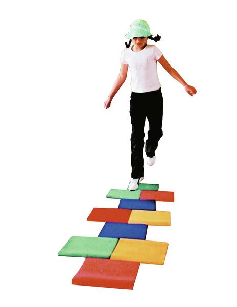 Kind spielt Hüpfspiel auf bunten Schaumstoffmatten, trägt weißen Hut und schwarze Hose.