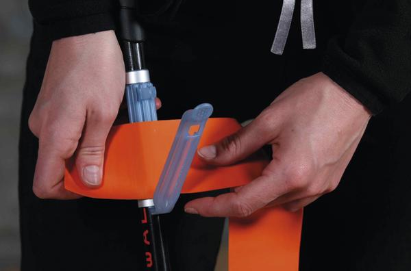 Person befestigt eine orangefarbene Skistöcke-Schutzmanschette an einem Skistock.