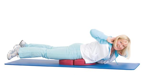 Frau macht Rückenübung auf Matte mit Kissen zur Stärkung der Rückenmuskulatur.