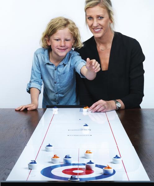 Kind und Frau spielen gemeinsam ein Tisch-Curling-Spiel und schieben Spielsteine auf die Zielscheibe.