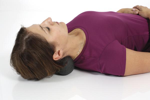 Frau liegt auf dem Rücken und verwendet einen Massageball im Nackenbereich zur Entspannung und Lockerung der Muskulatur.