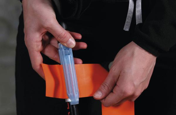 Person befestigt orangefarbenes Klebeband an einem schwarzen Gegenstand, Nahaufnahme der Hände.