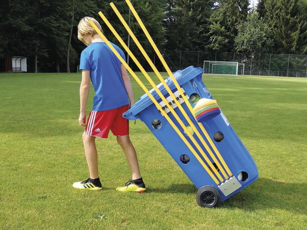 Junge zieht blauen Sportwagen mit Trainingshütchen auf grünem Fußballfeld.
