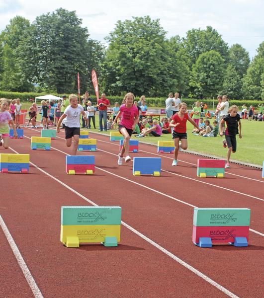 Kinder beim Hürdenlauf auf einer Sportbahn bei einem Leichtathletik-Wettbewerb im Freien.