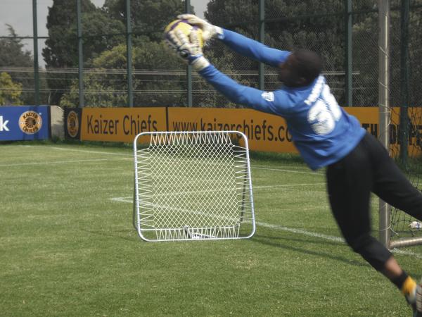 Torwart fängt Fußball im Sprung während Training auf grünem Spielfeld.