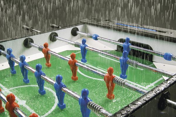 Tischkicker mit blauen und roten Figuren bei starkem Regen draußen.
