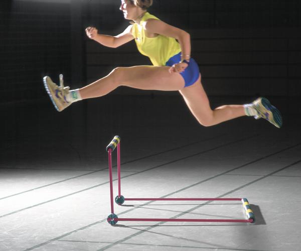 Frau springt über Hürde in Sporthalle, athletisch und dynamisch beim Training.